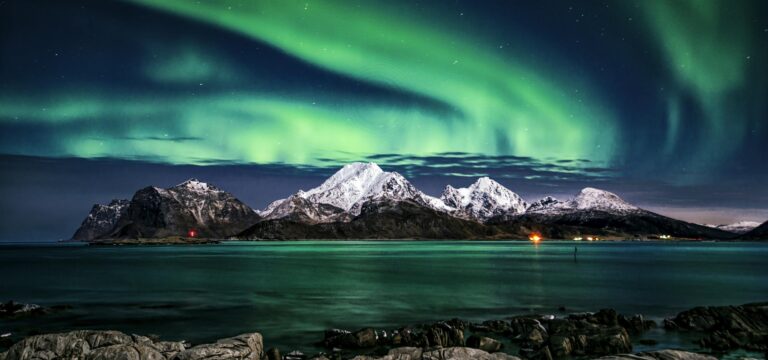 Breathtaking view of aurora borealis illuminating the snowy mountains of Lofoten Islands at night.